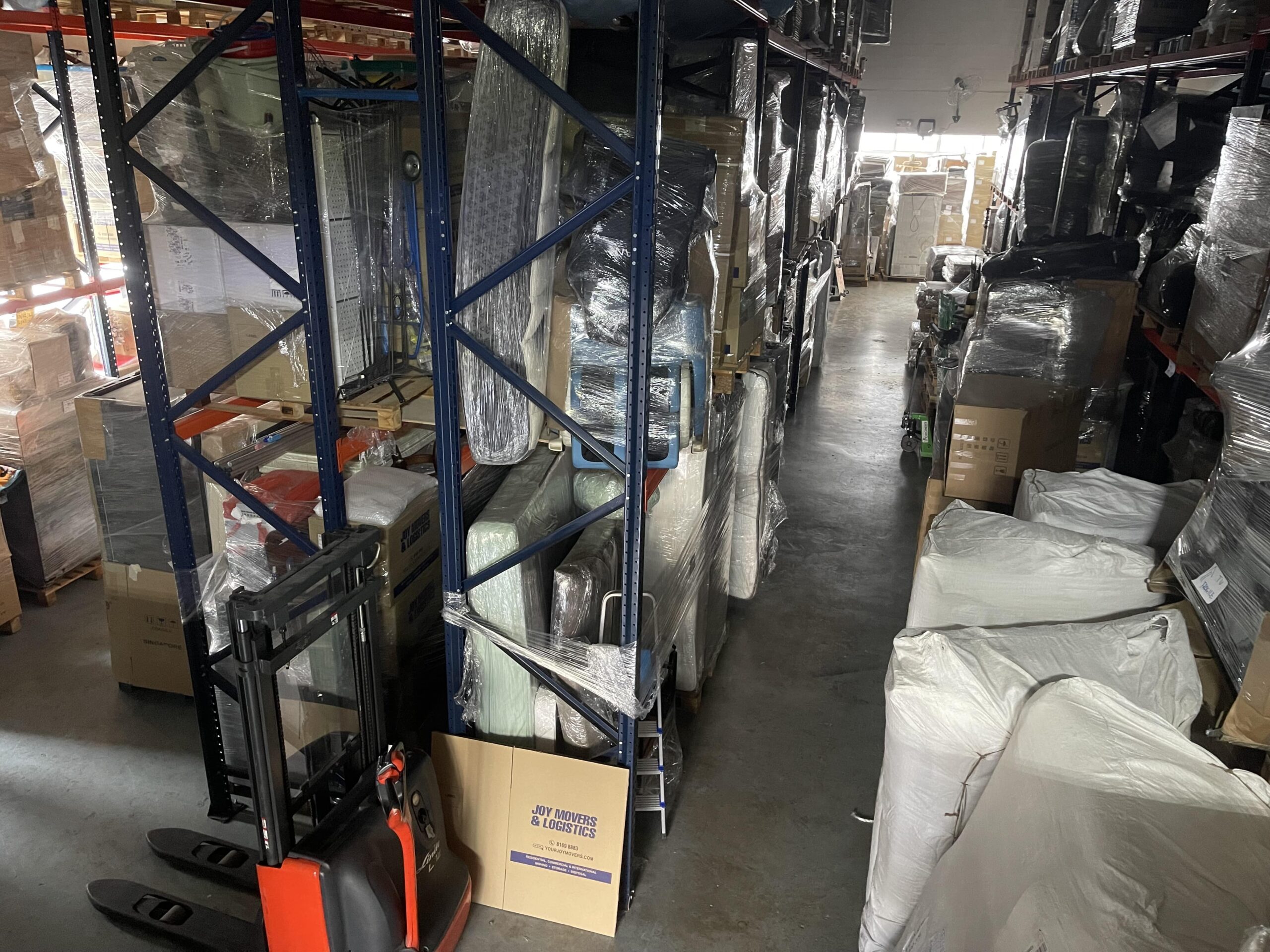 A moving company warehouse with tall metal shelving units filled with various wrapped items and boxes.