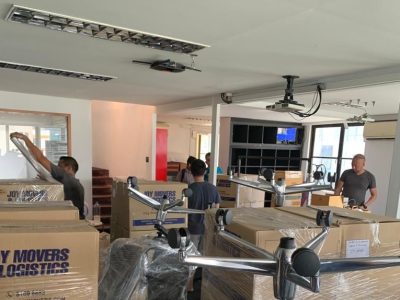 Several movers are packing and organizing cardboard boxes and office furniture in a well-lit room.